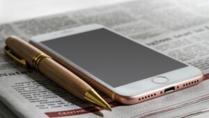 An iPhone and a pen sit on top of a folded newspaper